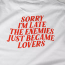 White t-shirt with red text 'Sorry I'm late. The enemies just became lovers' on a white background